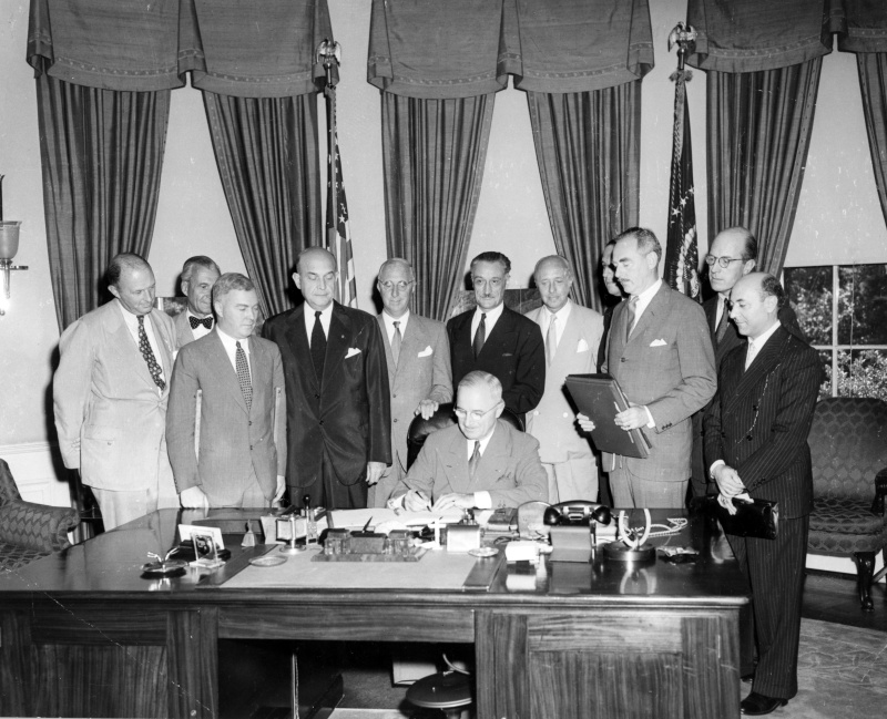 Former President Truman signs North Atlantic Treaty in the Oval Office with Portuguese ambassador Pedro Pereira and others serve as witnesses.