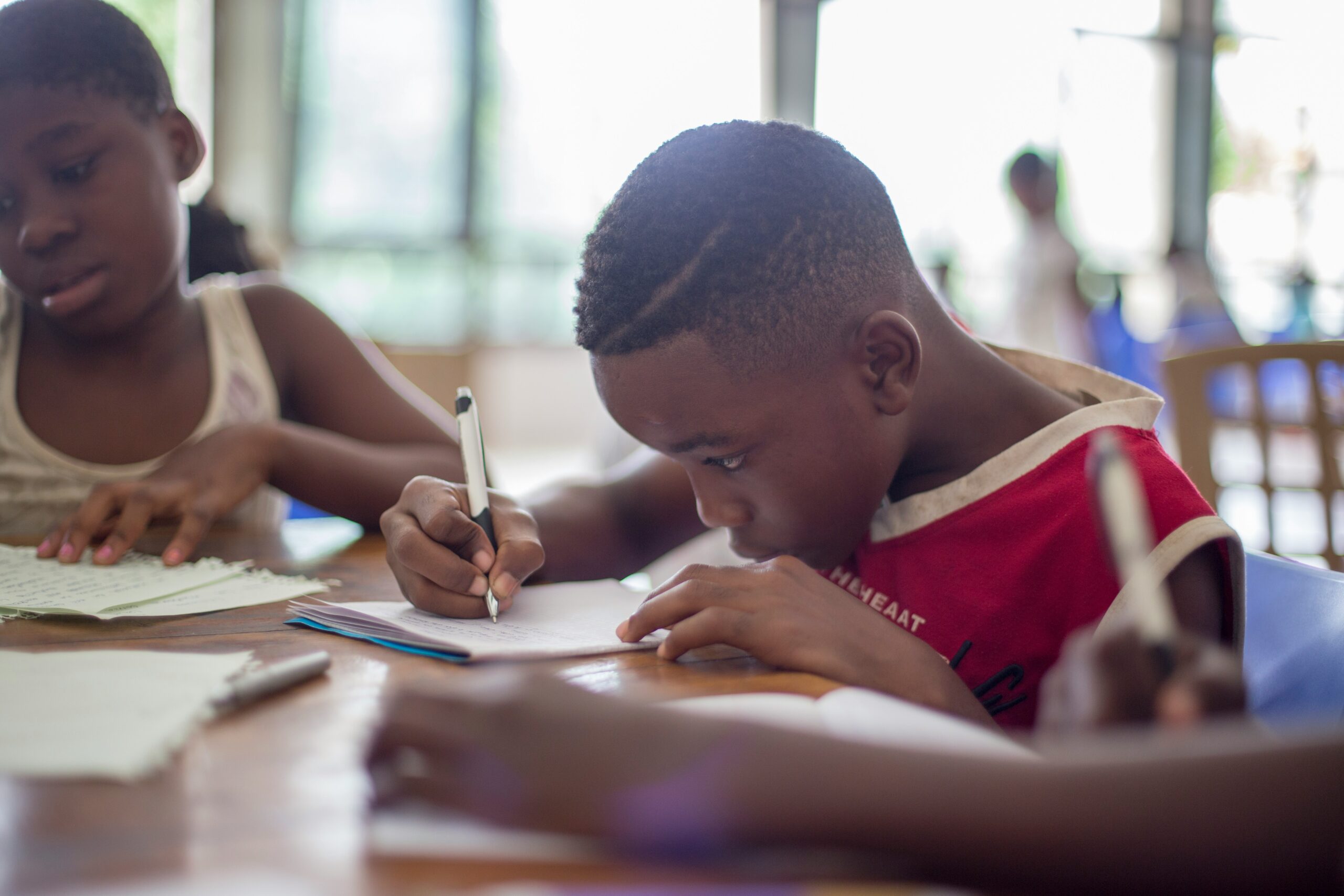 Boy writing on a piece of paper next to a girl.